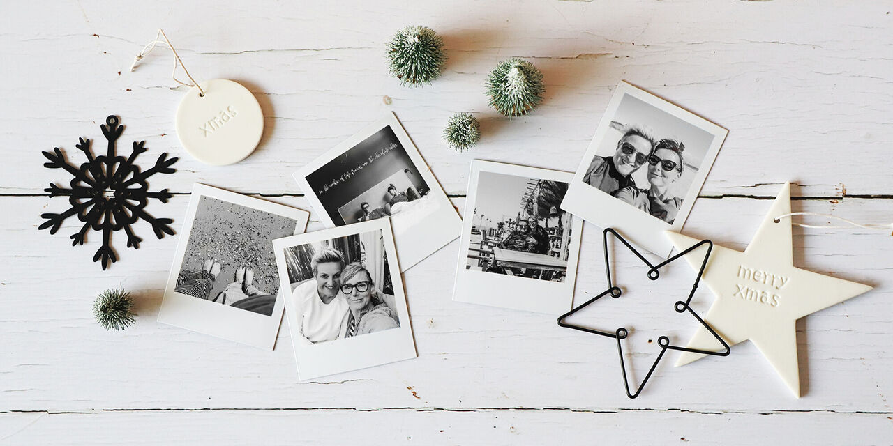 Auf einem Tisch liegen mehrere Fotomagnete mit schwarz-weissen Fotomotiven von zwei Freundinnen in den Ferien. Ringsherum liegen einige Weihnachtsanhänger ebenfalls in Schwarz und Weiss.