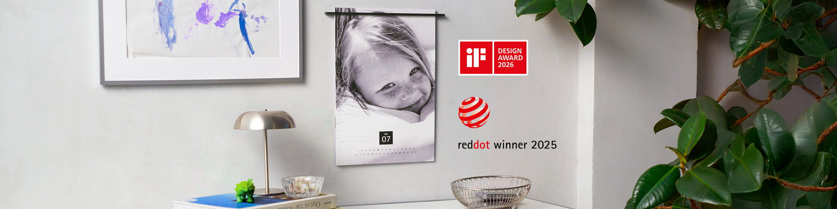 CEWE Fotokalender mit Schwarz‑Weiß‑Porträt eines Kindes hängt an der Wand, daneben Auszeichnungen iF Design Award 2026 und Red Dot Winner 20