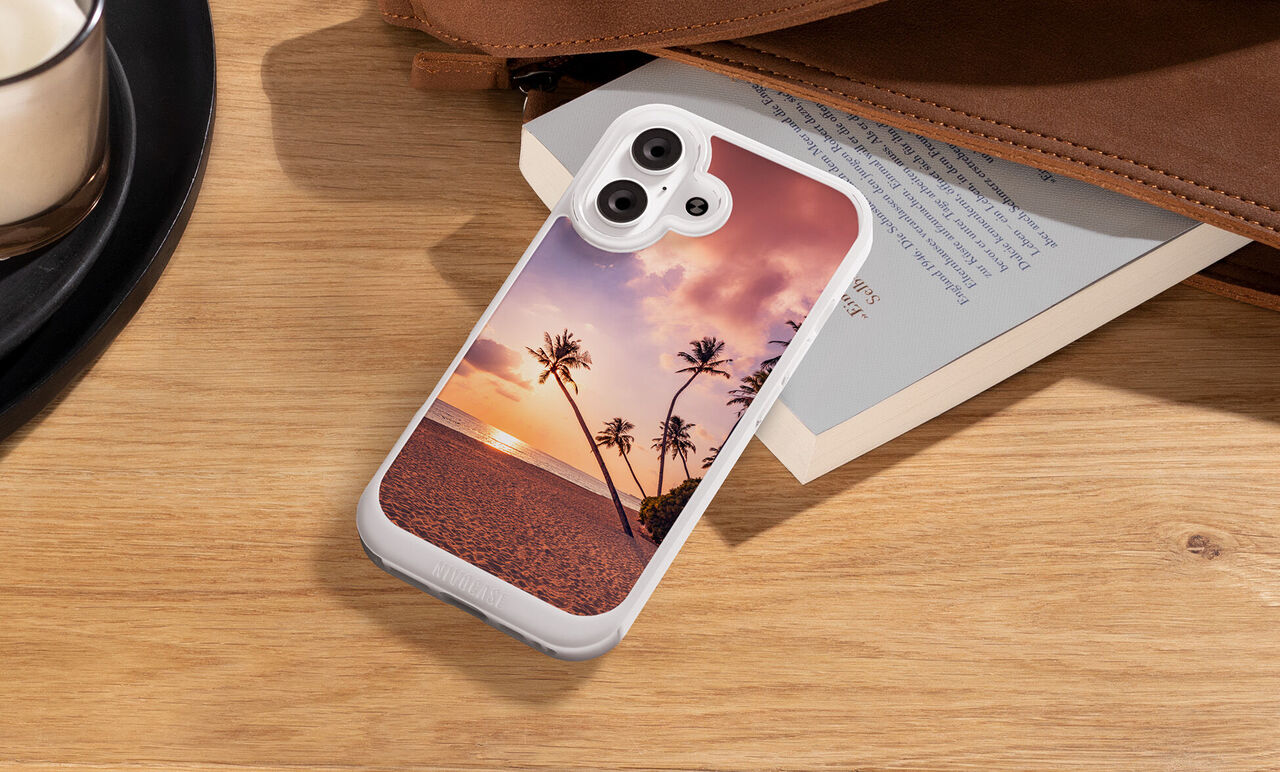 Smartphone Hülle liegt auf einem Holztisch auf einem Buch und zeigt ein Strandmotiv mit Palmen bei Sonnenuntergang