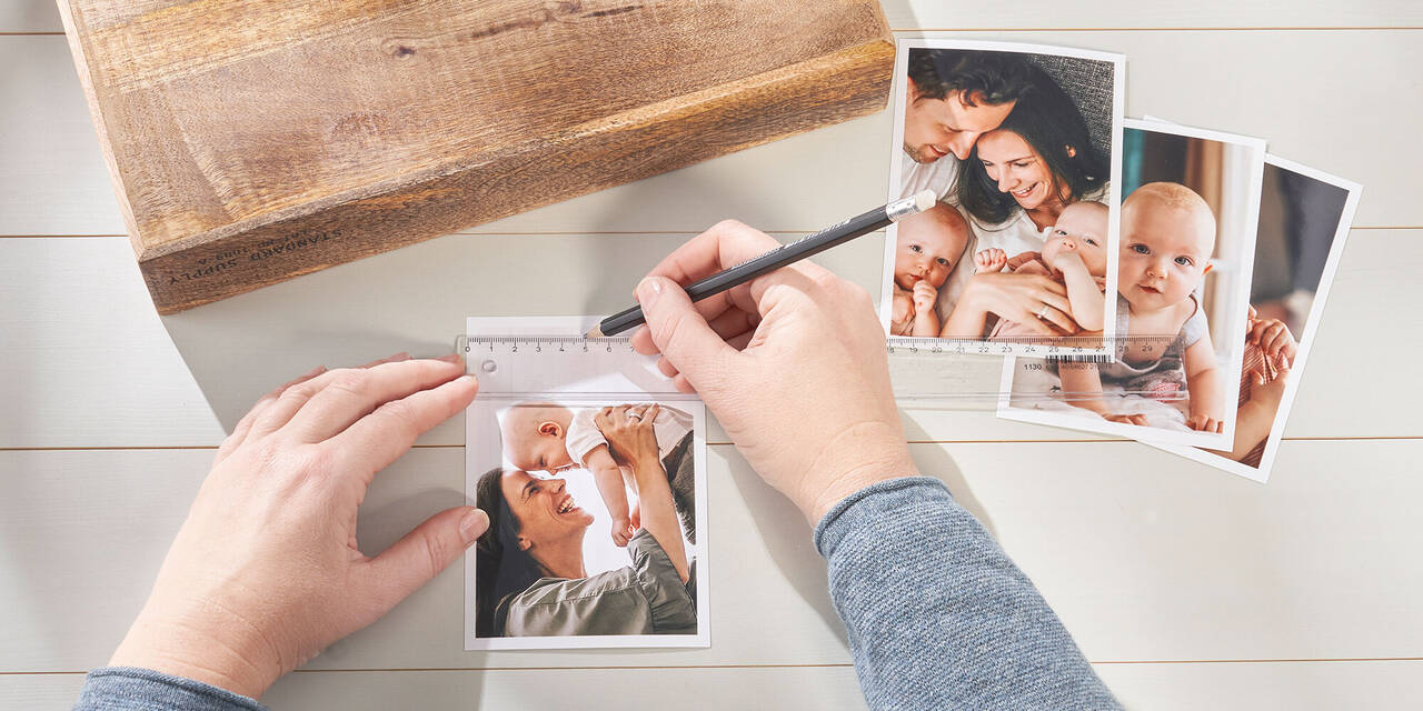 Aufnahme von zwei Händen, die mit Bleistift und Lineal eine Markierung auf einem CEWE Sofortfoto einzeichnen. Daneben liegen ein Holzblock und drei weitere Sofortfotos.