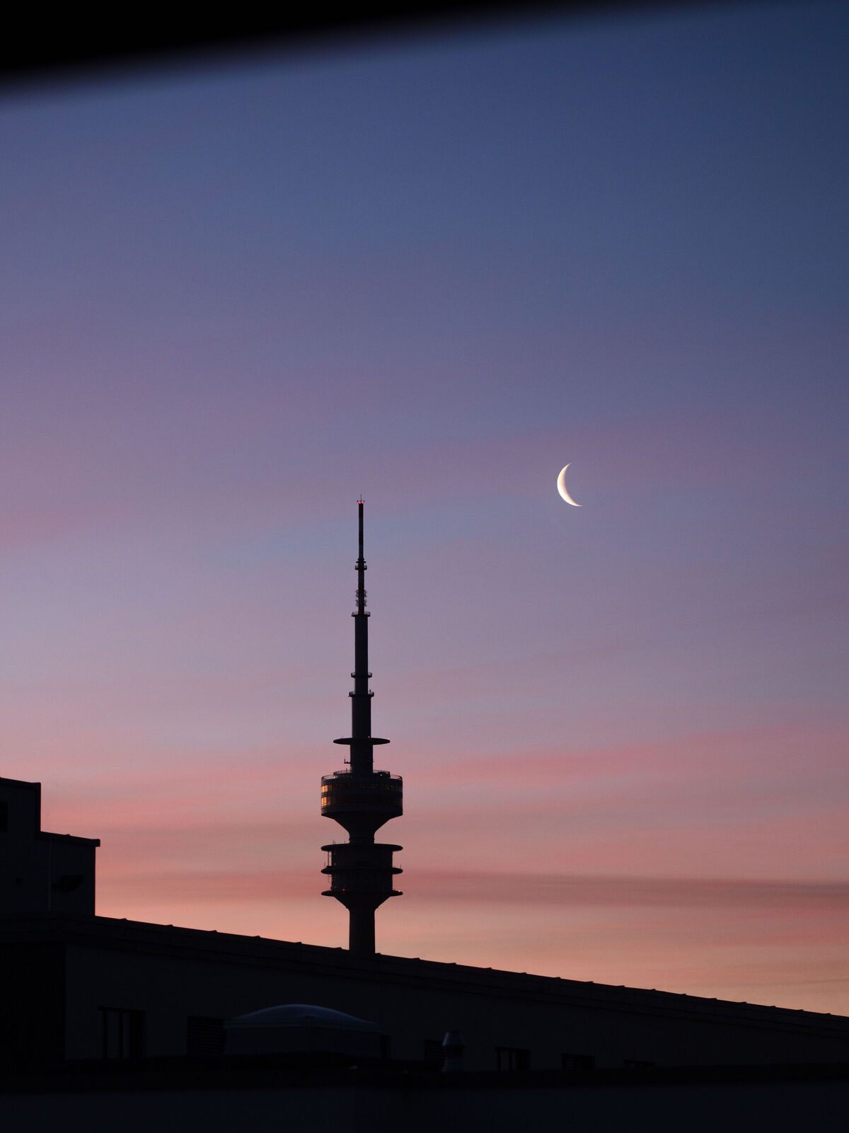 Schmale Mondsichel neben Funkturm am Abendhimmel mit rosa Wolken