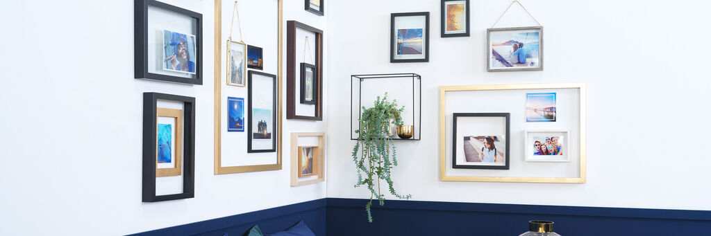 Ecksofa mit Esstisch. Mehrere unterschiedlich gerahmte Bilder hängen neben einem Regal, auf dem eine Pflanze steht.
