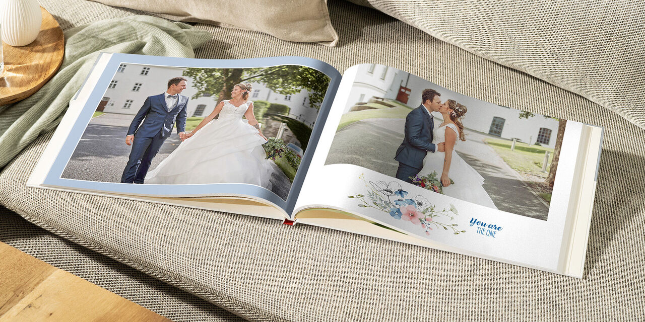 Un LIVRE PHOTO CEWE ouvert est posé sur un canapé de couleur claire. Sur la page de gauche, on peut lire « Our guests », on y voit les jeunes mariés avec leurs témoins. Sur la page de droite, les mariés sont accompagnés de leurs parents.