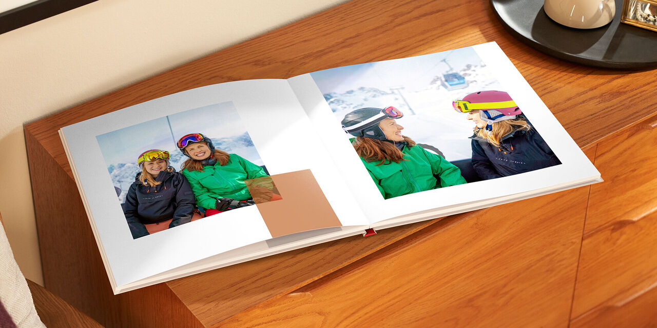 Il fotolibro aperto è appoggiato su un mobile di legno. Entrambe le pagine mostrano le foto di due donne sulla pista da sci.