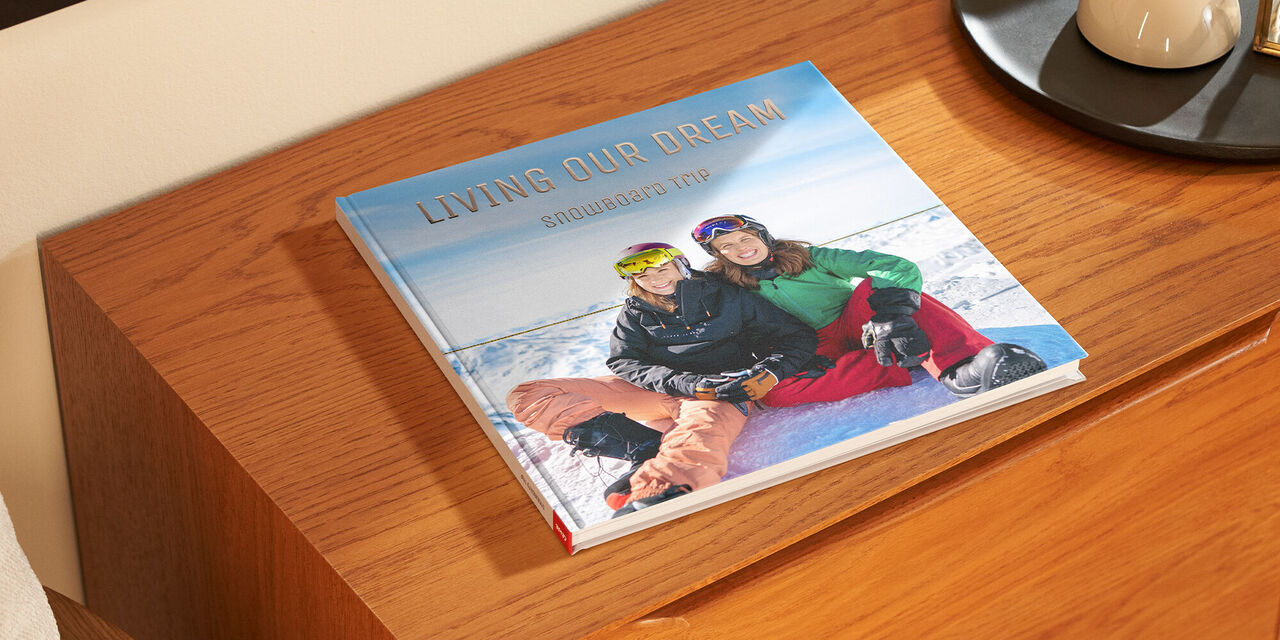 Un fotolibro chiuso è appoggiato su un mobile di legno. Sulla copertina c’è la foto di due donne nella neve. La didascalia «Living our Dream» è impreziosita da lettere dorate.