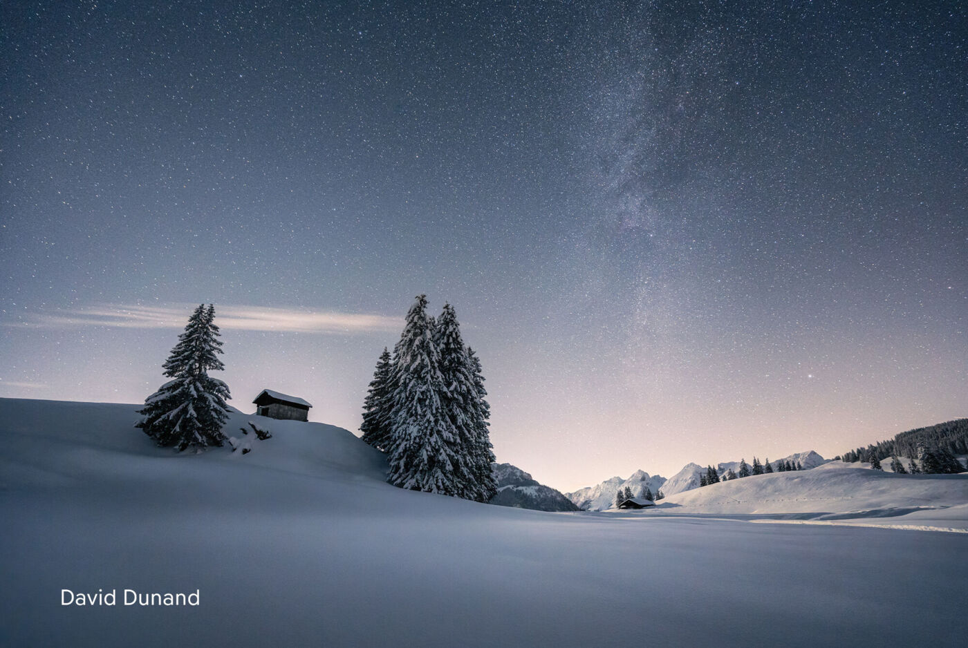 Un paesaggio invernale innevato sotto un cielo stellato con una piccola casa di legno circondata da alti abeti.